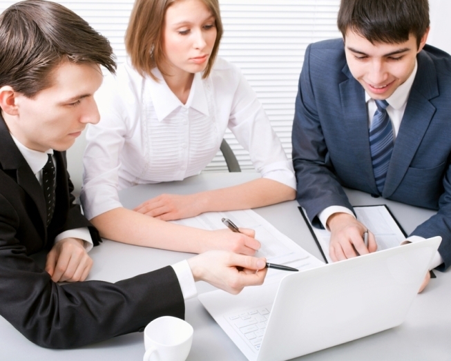 Placeholder image of 3 people sitting at a tale point at documents with their pens.